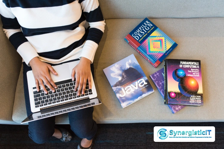 Person typing on laptop surrounded by Java programming books and computer science fundamentals.