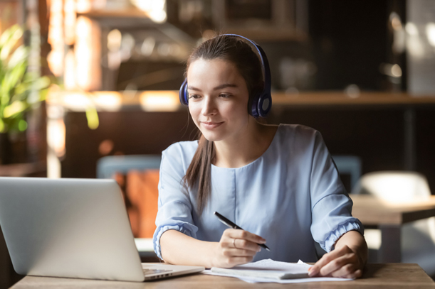 Woman wearing headphones studying Java online with laptop and pen.