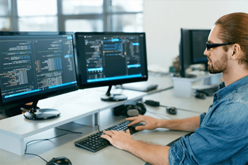 Man coding Java applications on dual monitors, SynergisticIT’s Job Placement Program training.