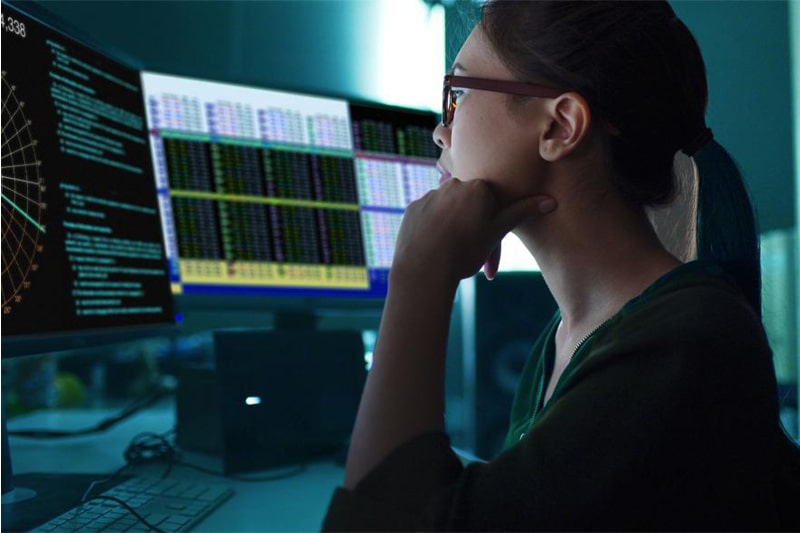 Woman analyzing data visualizations and code on multiple monitors, illustrating Data Science training in Oklahoma.