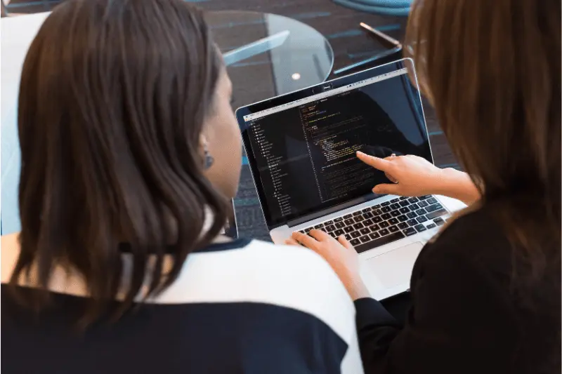 Two people reviewing Java code on laptop screen, illustrating IT skill enhancement and job placement