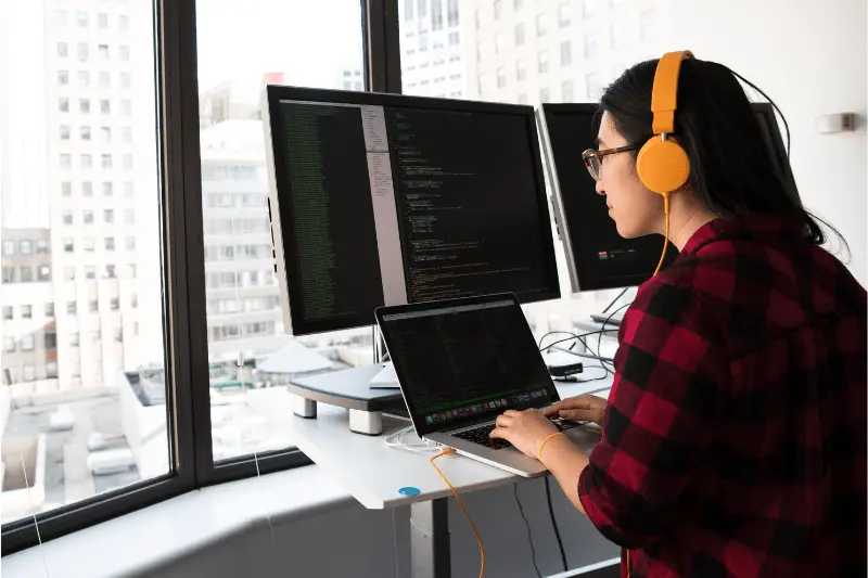 Woman coding on laptop and monitors, Java training and programming skills development.