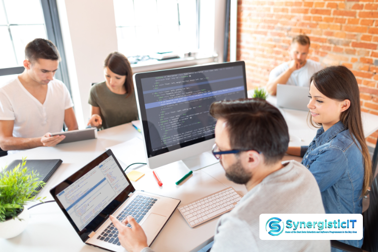 Software developers collaborating around computer screens with code and database interfaces.
