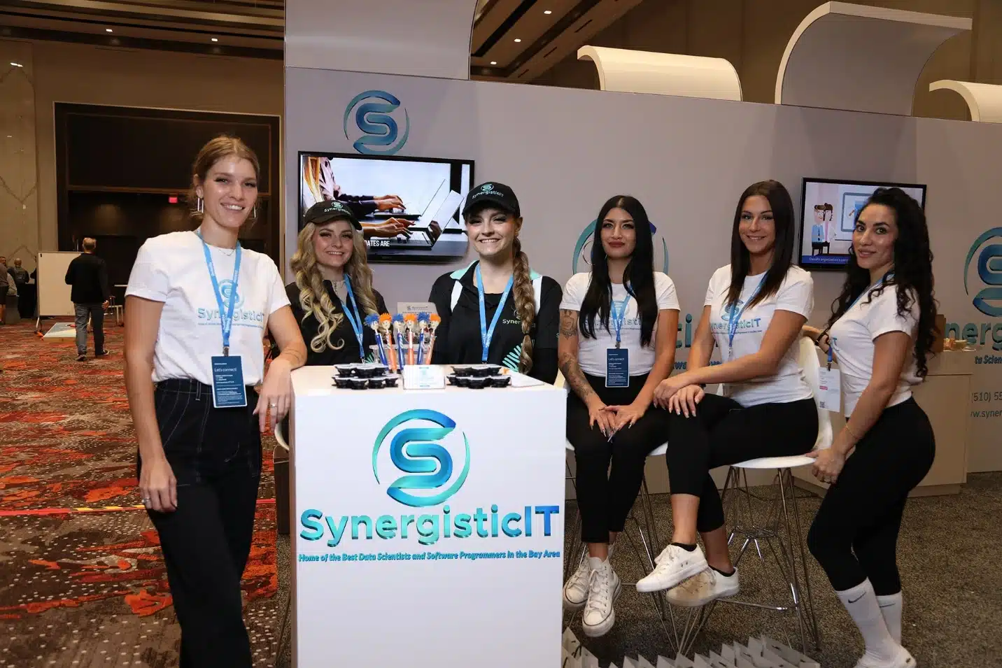 SynergisticIT team at tech conference booth promoting fraud-resistant talent sourcing.