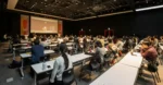 Bootcamp graduates versus computer science degree holders comparison chart and audience in a lecture hall.